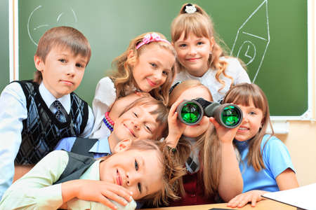 Happy schoolchildren at a classroom looking through binoculars. Education.の写真素材