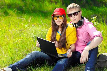 Couple of modern teenagers sitting with a laptop outdoors.の写真素材