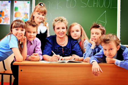 Happy schoolchildren with their teacher at a classroom.の写真素材
