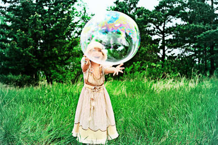 Pretty little girl is playing with big bubbles in a park.の写真素材