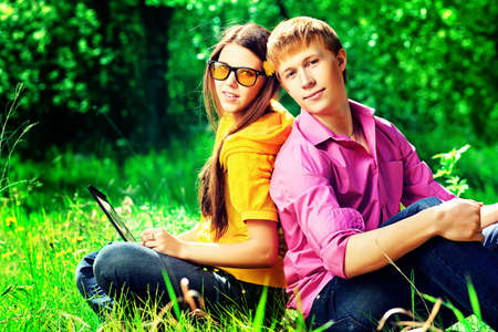 Couple of modern teenagers sitting with a laptop outdoors.の写真素材