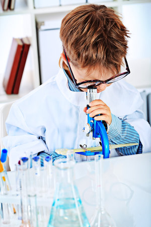 Cute boy is lookingin his microscope in a laboratory. Education.