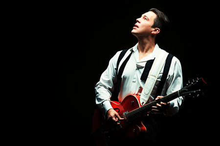 Portrait of a professional artist playing on guitar. Over black background.