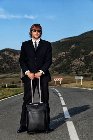 Handsome business man standing on a highway with his suitcase.の写真素材