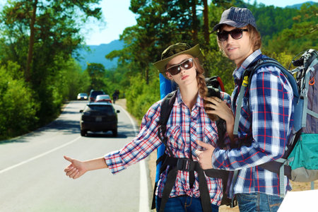 Two young people tourists hitchhiking along a road.の写真素材