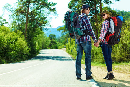 Two young people tourists hitchhiking along a road.