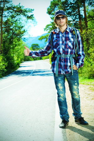 Young man tourist hitchhiking along a road.
