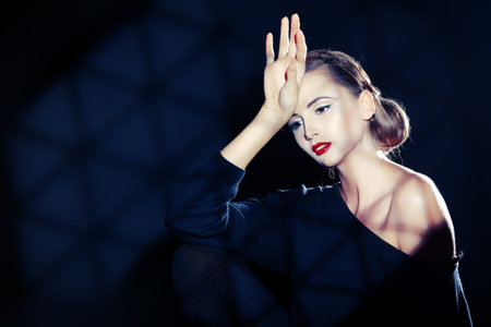 Elegant young woman in black clothes posing at studio. Light and shadow.