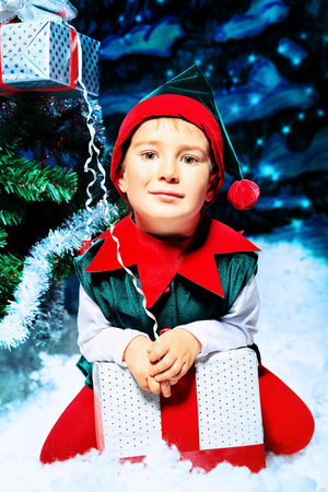 Little boy in Christmas elf costume posing over christmas background.
