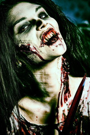 Bloodthirsty zombi with a knife standing at the night cemetery in the mist and moonlight.