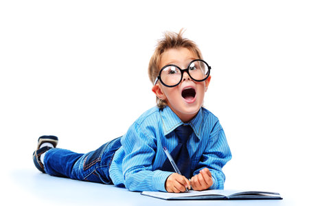 Little boy in spectacles and suit lying on a floor with a diary. Isolated over white background.
