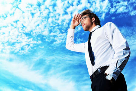 Successful business man standing over blue sky and purposefully looking away.の写真素材