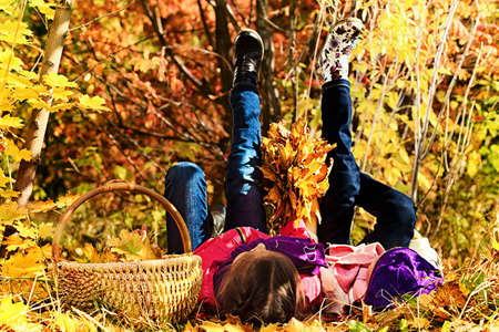 Portrait of two cute girls sisters lying on the leaves at the autumn park.の写真素材