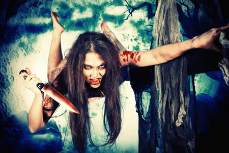 Bloodthirsty zombi with a knife at the night cemetery in the mist and moonlight.の写真素材