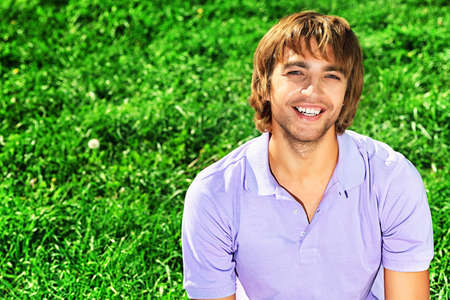 Happy smiling young man sitting on a fresh green grass.の写真素材