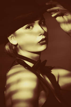 Elegant young woman posing in vest and black pot hat. Light and shadow.の写真素材