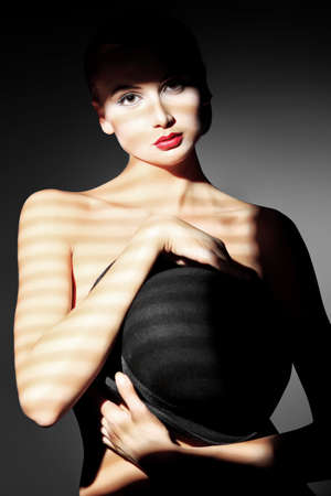Elegant naked young woman posing with black pot hat. Light and shadow.の写真素材