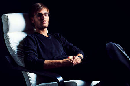 Portrait of a handsome man sitting in the armchair over black background.の写真素材