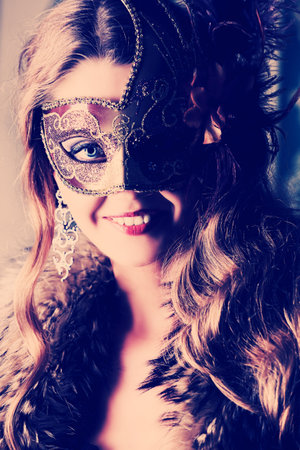 Beautiful young woman in a carnival mask over vintage background. 