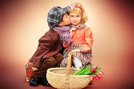 Cute little boy and girl are sitting with a basket of tulips. Retro style.の写真素材