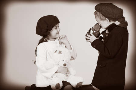 Cute little boy is photographing the charming little lady with his old camera. Retro style.の写真素材