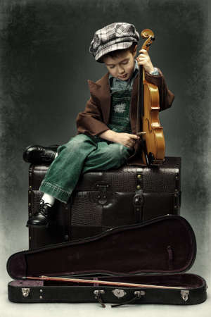 Portrait of a little boy sitting on a big old trunk with his violin. Retro style.の写真素材