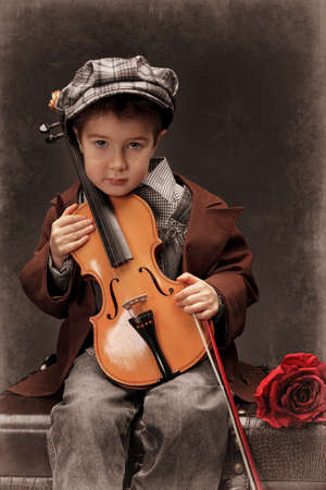 Portrait of a little boy sitting on a big old trunk with his violin. Retro style.の写真素材