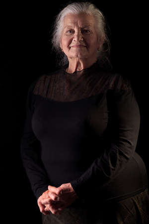 Portrait of a happy senior woman smiling at the camera. Over black background.の写真素材