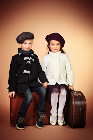 Cute little boy and girl are sitting on their old suitcases. Retro style.の写真素材