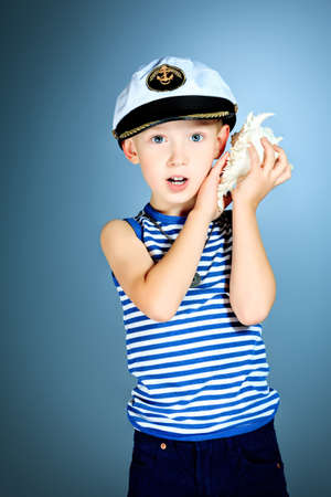 Little smiling sailor boy is listening to the sound of the sea in the shell.の写真素材
