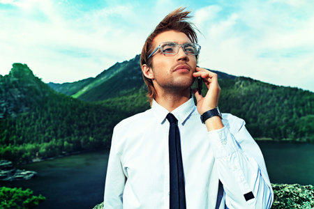 Successful business man standing on a peak of the mountain and talking on the phone.の写真素材