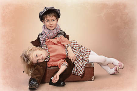 Cute little boy is sitting on the old suitcase with charming little lady. Retro style.の写真素材
