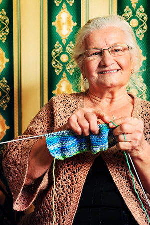 Portrait of a smiling senior woman knitting on spokes at home. Old-fashioned style.の写真素材