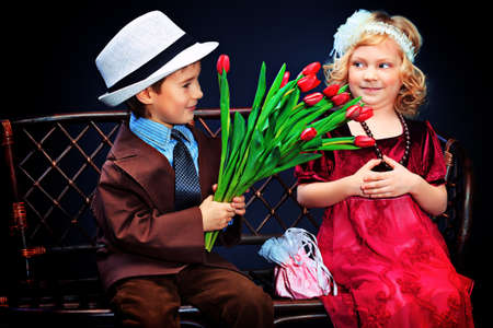 Cute little boy is giving bouquet of tulips to the charming little lady. Retro style.の写真素材
