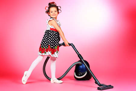 Portrait of a cute little pin-up girl with a vacuum cleaner over pink background.の写真素材