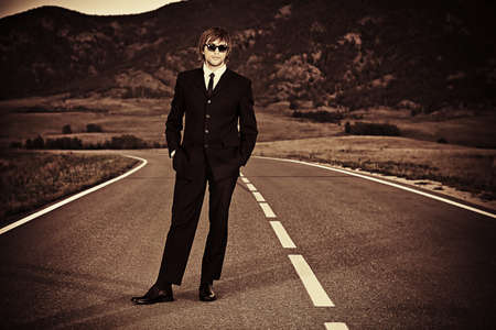 Handsome business man in a black suit standing on a highway.の写真素材