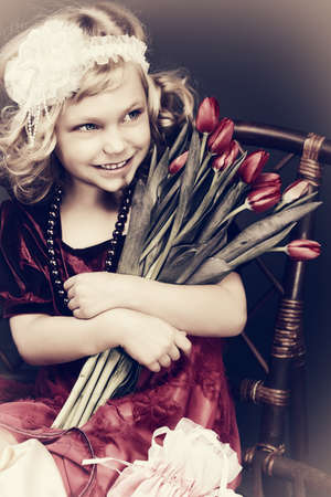 Portrait of a charming little lady with a bouquet of tulips sitting on a bench. Vintage style.の写真素材