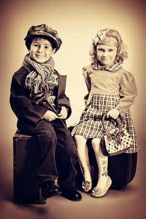 Cute little boy is sitting on the old suitcase with charming little lady. Retro style.の写真素材