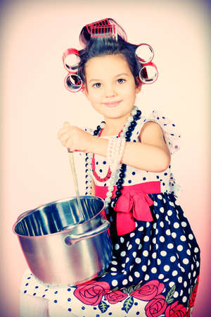 Portrait of a cute little pin-up girl with a pan over pink background.の写真素材