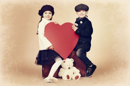 Cute little boy holding red heart with a charming little girl. Retro style.の写真素材