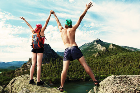 Couple of tourists are standing at the top of a mountain with a feeling of freedom.