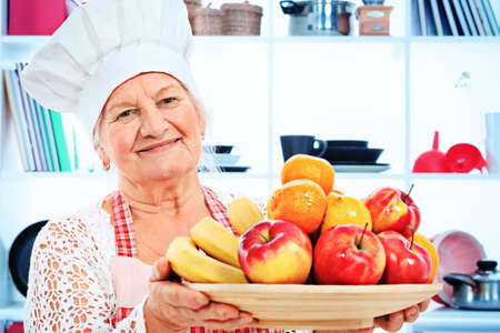 Senior woman chef cook standing with a plate of fruits in the kitchen.の写真素材