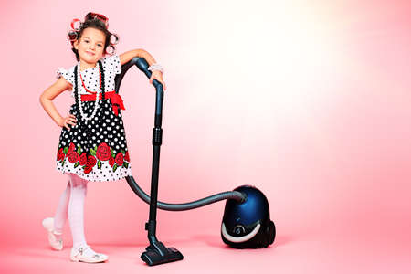 Portrait of a cute little pin-up girl with a vacuum cleaner over pink background.の写真素材
