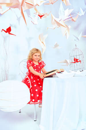 Beautiful little girl dreaming with her book and red paper bird in a birdcage.の写真素材