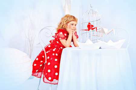 Portrait of a beautiful little girl holding birdcage with a red paper bird.の写真素材