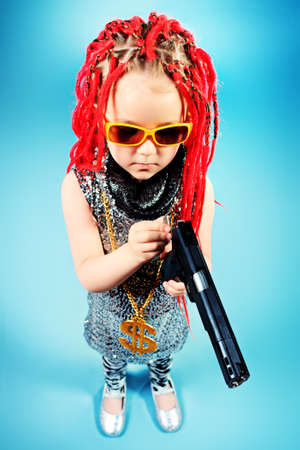Portrait of a trendy little girl wearing red braids and modern clothes and holding a gun.の写真素材