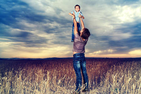 Happy father playing with his little son in the wheat field over beautiful cloudy sky. の写真素材