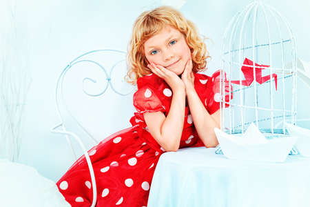 Portrait of a beautiful little girl holding birdcage with a red paper bird.の写真素材