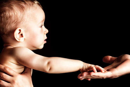 Baby is holding father's hand. Over black background.の写真素材