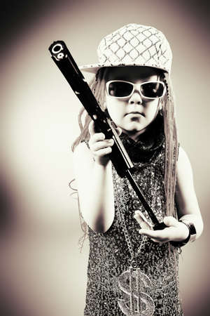 Portrait of a trendy little girl wearing red braids and modern clothes and holding a gun.の写真素材
